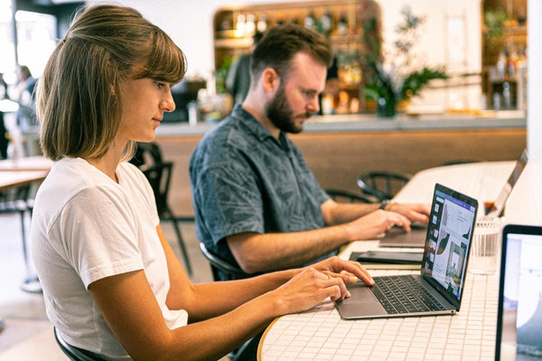 Two people sitting at a table using laptops.